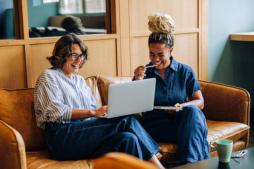 Two women sharing a laugh while using a laptop in a cozy setting