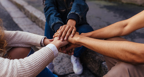 Group of friends sitting together stacking their hands on one another
