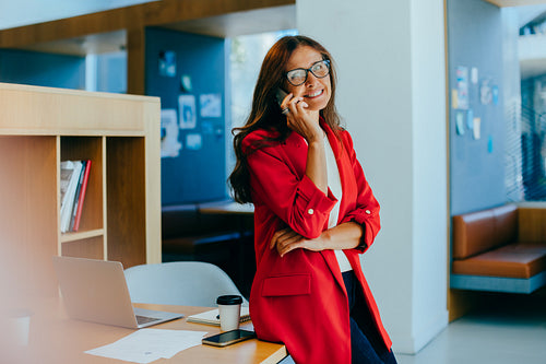 Confident businesswoman in red jacket talking on phone in an office environment
