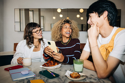 Three friends laughing together at a cafe table