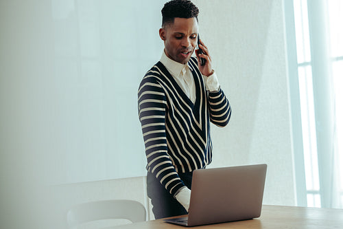Confident black male business owner talking on the phone while working