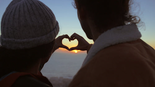 Couple making heart with hands looking at sun
