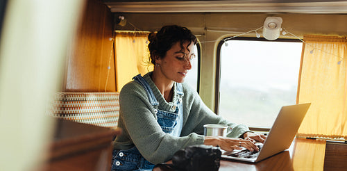 Quiet work session: Woman typing on her laptop inside a cozy camper van