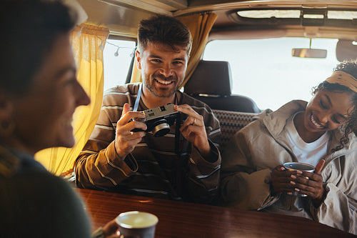 Friends on a road trip share smiles as a man photographs inside a van