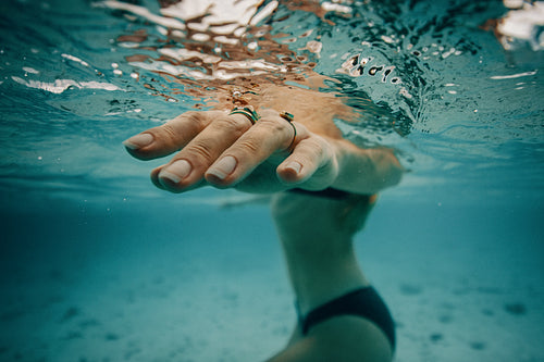 Hand of a woman underwater wearing rings in a clear blue ocean