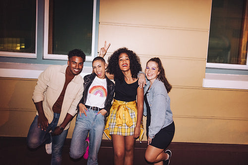 Happy friends standing against a wall at night