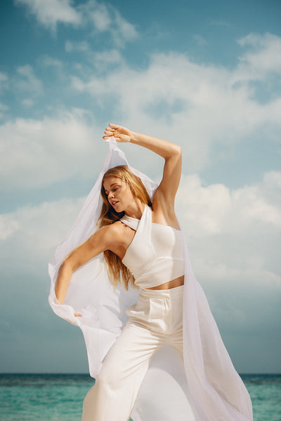 Woman dancing elegantly on a beach with white fabric flowing in the breeze