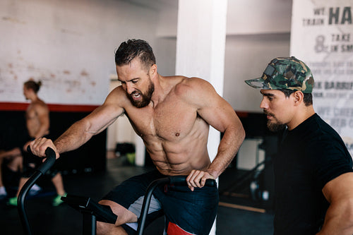 Muscular man exercise on stationary bike with personal coach
