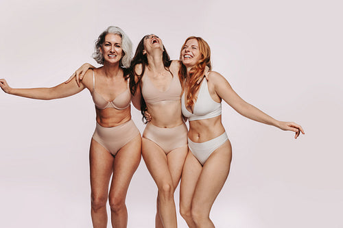Three women in underwear hug and laugh in studio