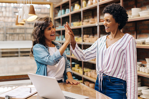 Successful female ceramists high fiving each other in their shop