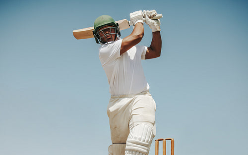 Male cricket batsman playing a powerful shot against a clear blue sky