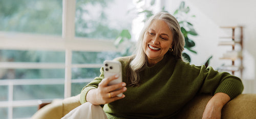 Senior woman uses a smartphone while relaxing at home