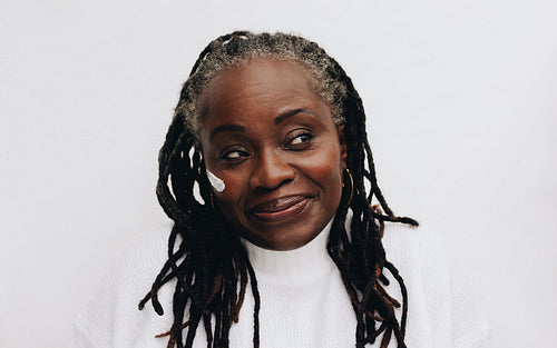 Mature woman with dreadlocks applying a beauty cream on her face