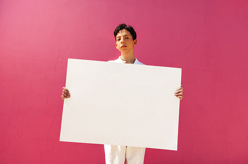 Confident queer boy holding a blank placard against a pink background