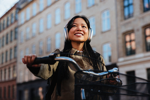 Woman riding bicycle in city wearing headphones and smiling