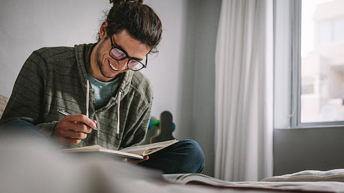 Smiling student studying for exam sitting on bed