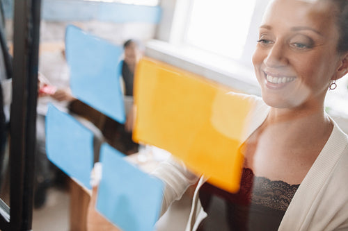 Business woman sticking adhesive notes on glass wall