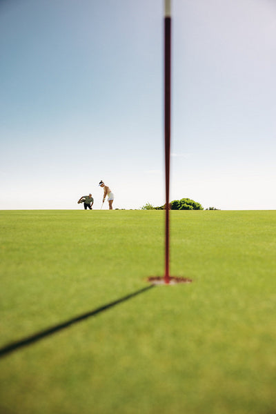 Woman golfer aiming at the hole in the background focusing on the flagstick