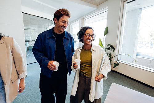 Two colleagues laugh while sharing coffee in the office