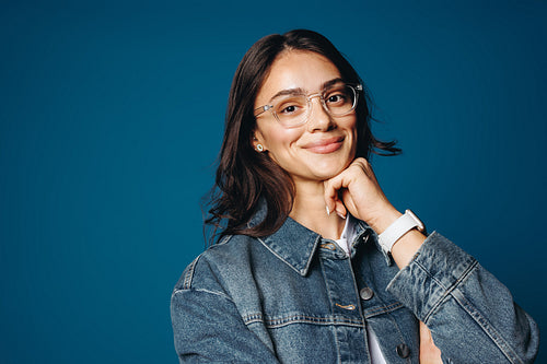Young entrepreneur posing confidently in studio with denim jacket and glasses