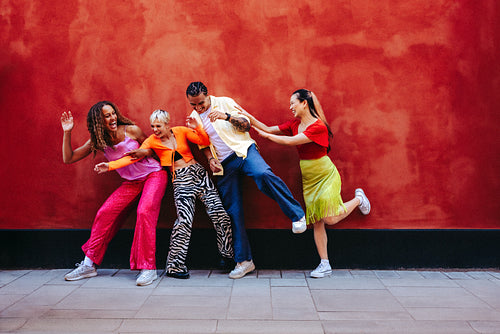 Playful group of friends having fun against a red wall outdoors