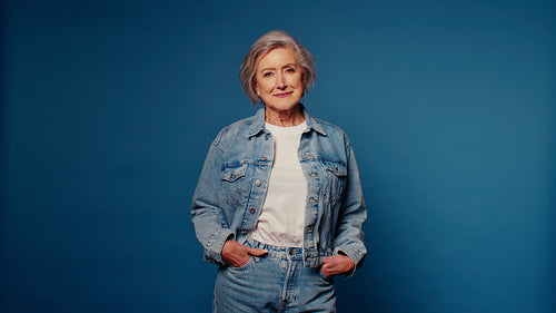 Confident senior woman in denim poses against a blue studio background