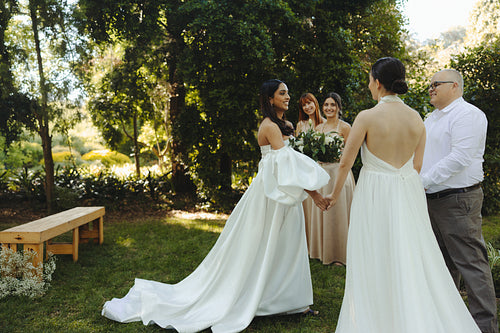 Lesbian couple exchanging vows in an outdoor wedding ceremony surrounded by guests