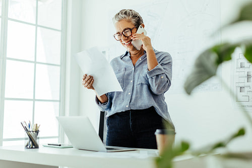 Happy design professional reviewing a document and talking to a client over the phone