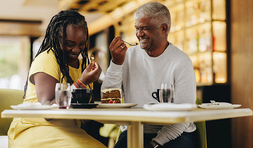 Cheerful senior couple eating a cake together in a restaurant