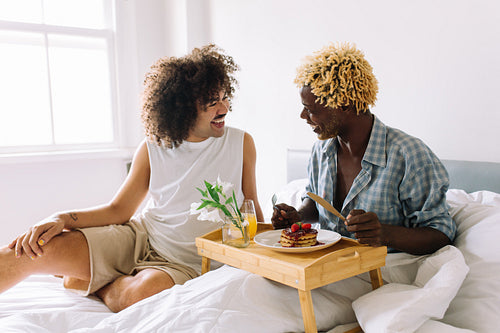 Cheerful gay man eating breakfast in bed