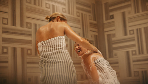Mature woman and younger woman enjoying pampering together in a hammam. Relaxing spa experience with laughter and bonding.