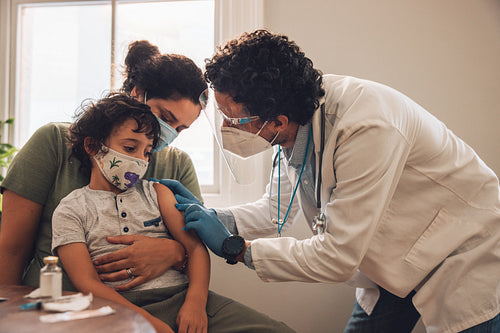 Doctor giving vaccine to a small boy with mother at home