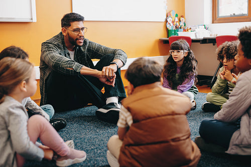 Teacher sitting on the floor with his students in an elementary school classroom