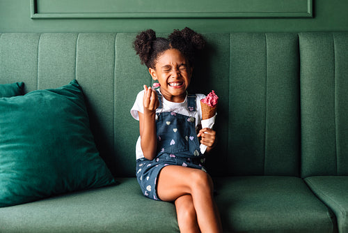 Happy young girl laughing with ice cream on green sofa