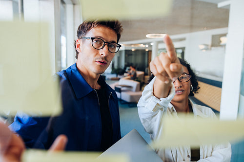 Tech professionals review sticky notes on glass wall