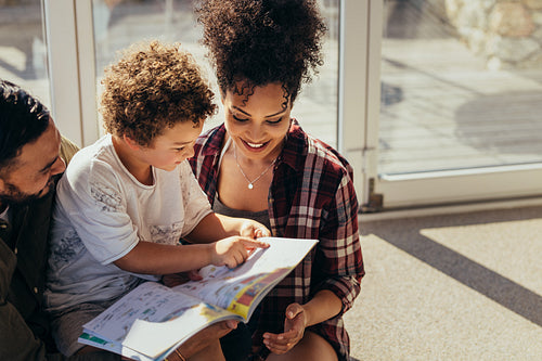 Kid reading a story book sitting with his parents