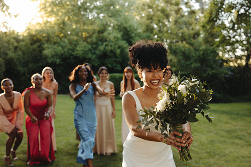 Bride tossing her bouquet surrounded by friends outdoors