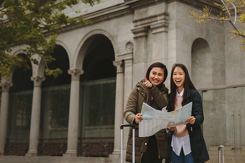 Two female tourists standing on street holding a city map