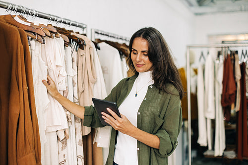 Shop owner uses a tablet to do a quality control check in her clothing boutique