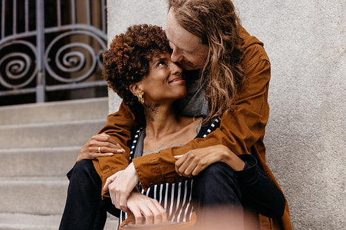 Affectionate embrace on city steps, joyful rendezvous of diverse couple