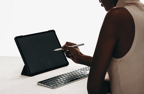 Woman using stylus on digital tablet with keyboard for mockups and creative work
