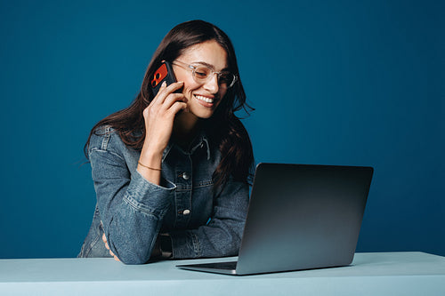 A woman handles work while talking on her smartphone on a blue background setup