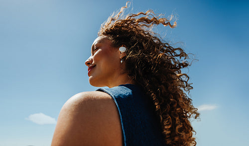 Woman enjoys music with earbuds under a clear blue sky