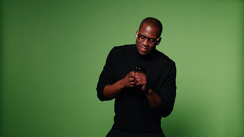 Stylish man dances to music on his phone against a green screen