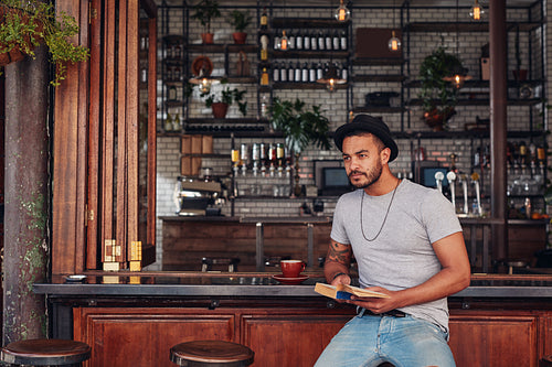 Trendy young male sitting at a cafe counter with a book