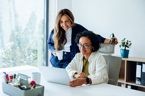 Manager overseeing employee work on laptop in modern office