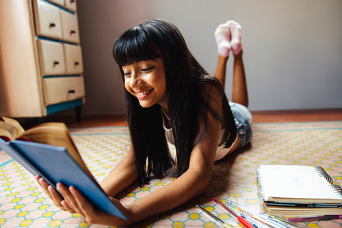 Young girl enjoying reading a book while lying comfortably at home