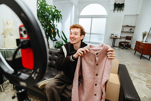 The camera captures a fashion seller as he presents clothing for online promotion.