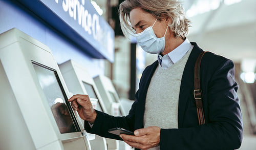 Business traveler with mask using self service check in at airpo