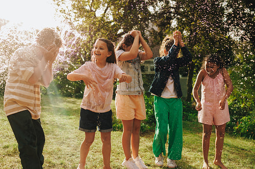 Group of children playing with water splash outdoors on a sunny day